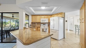 A modern kitchen with granite countertops, white cabinets, a built-in microwave, and a refrigerator. - Cozy Retreat, pool, fresh water canal, bbq grill , fire pit, electric bikes. (Cape Coral)