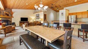 A spacious living area with a wooden ceiling, a large dining table, and comfortable seating. - Woodbine Cabin | Big Sky (Big Sky)