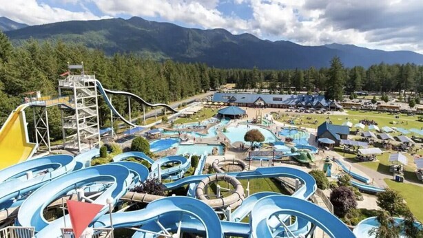 Un parc aquatique doté de nombreux toboggans et d’un grand espace piscine, le tout entouré de montagnes et d’arbres.