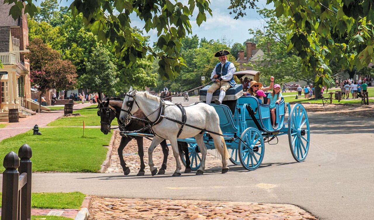 A horse-drawn carriage with passengers, a building with a brick facade, and a tree-lined street.