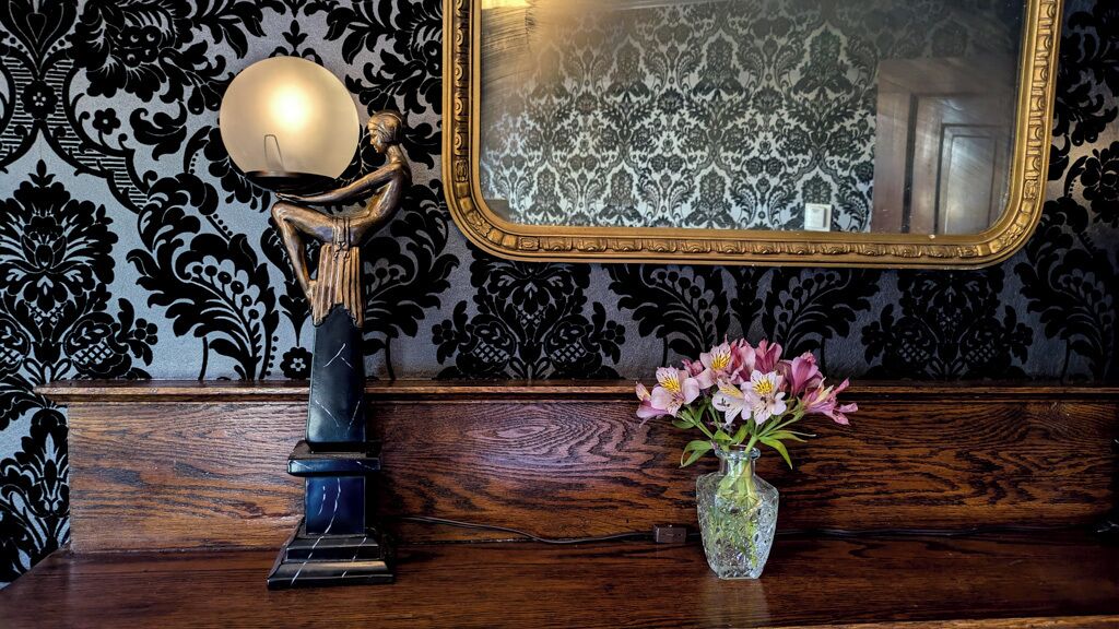 Eine hölzerne Bank mit Blumen in einer Vase und einer Lampe mit einer kugelförmigen Lichtquelle.
