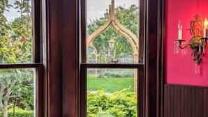 A room with a view of a garden through a stained glass window, a wooden door, and a wall-mounted light fixture. - The Weller House (Fort Bragg)