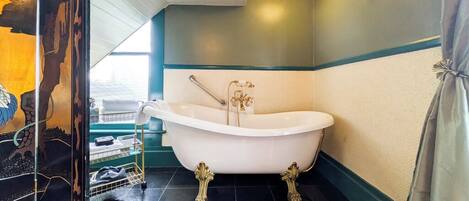 A bathroom with a freestanding bathtub, a towel rack, and a window with a view of the sea.