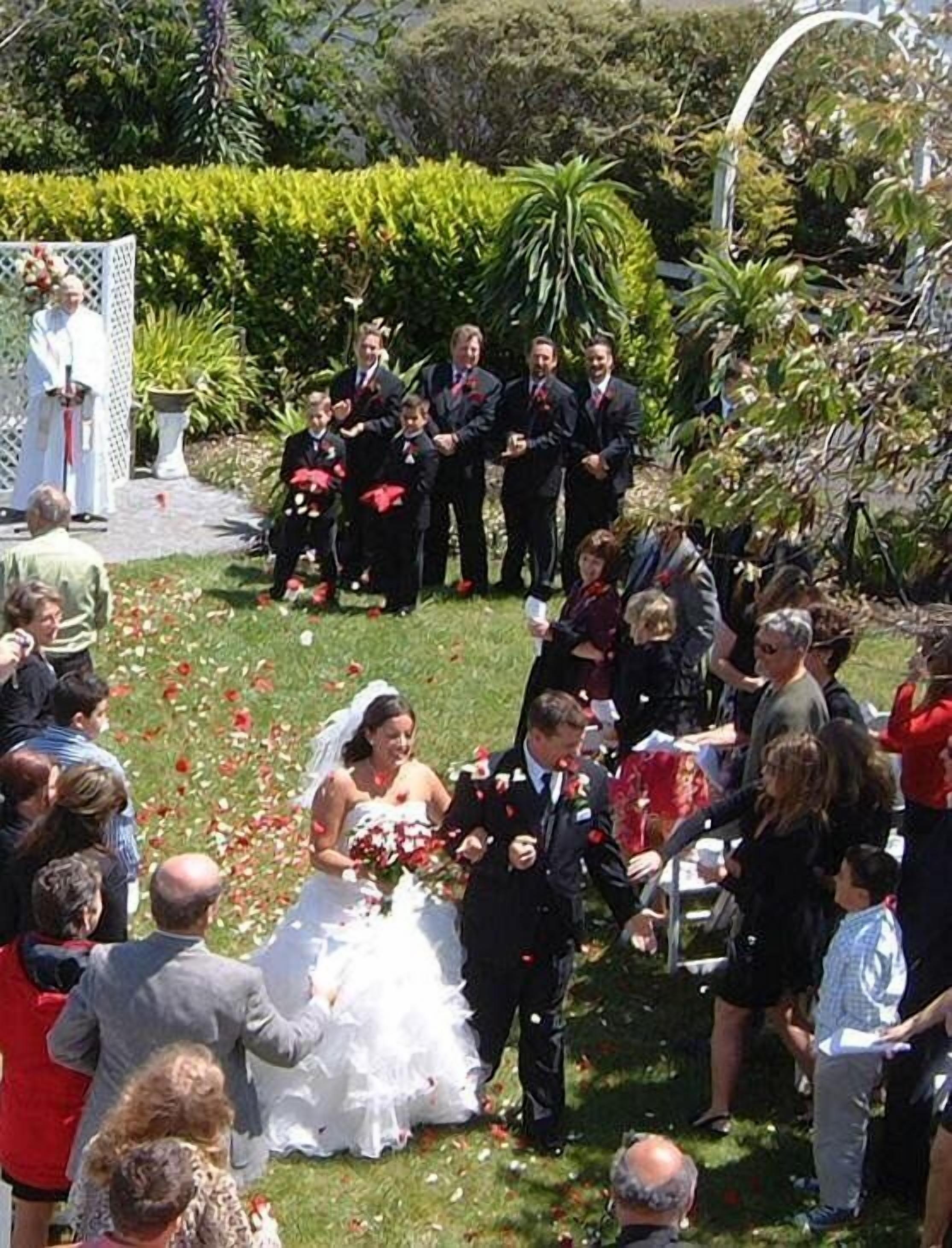 Una ceremonia de boda al aire libre con invitados sentados y de pie alrededor de la pareja.
