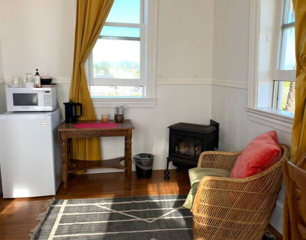 A compact kitchen with a microwave, a small table, and a wicker chair.