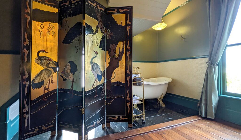 A traditional Japanese-style bathroom with a wooden floor, a white bathtub, and a decorative screen with nature motifs.