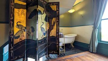 A traditional Japanese-style bathroom with a wooden floor, a white bathtub, and a decorative screen with nature motifs.