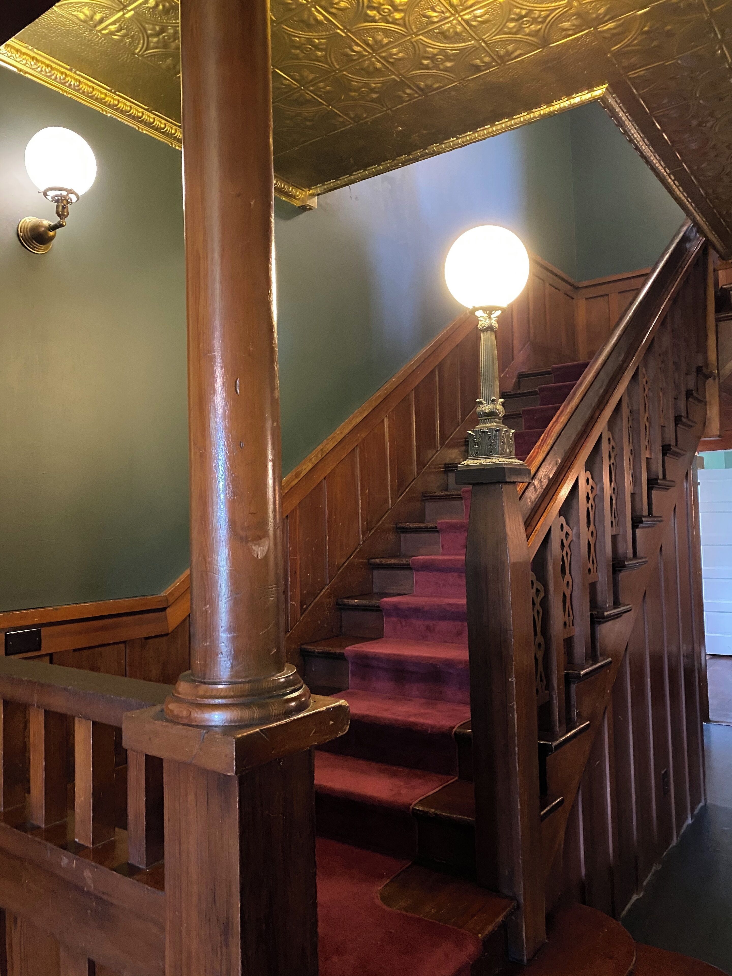 A wooden staircase with a handrail, carpeted steps, and a wall with a decorative pattern.