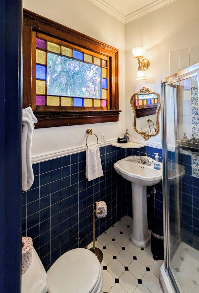A bathroom with a white toilet, a pedestal sink, a glass shower enclosure, and a stained glass window above the sink.