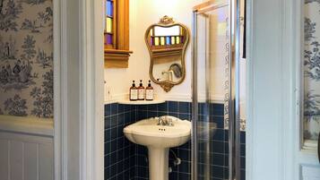 A bathroom with a pedestal sink, a mirror, and a shower.