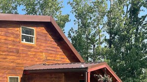 A wooden cabin with a red porch and a small staircase leading to a deck. - Cedar Cabin Cozy 2-Bedroom next to Glacier Park (East Glacier Park)