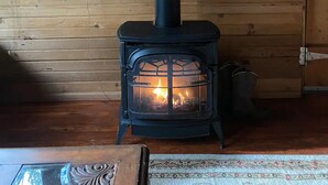 A wood-burning stove with a glass door, flanked by two woven baskets on the wall. - Cedar Cabin Cozy 2-Bedroom next to Glacier Park (East Glacier Park)