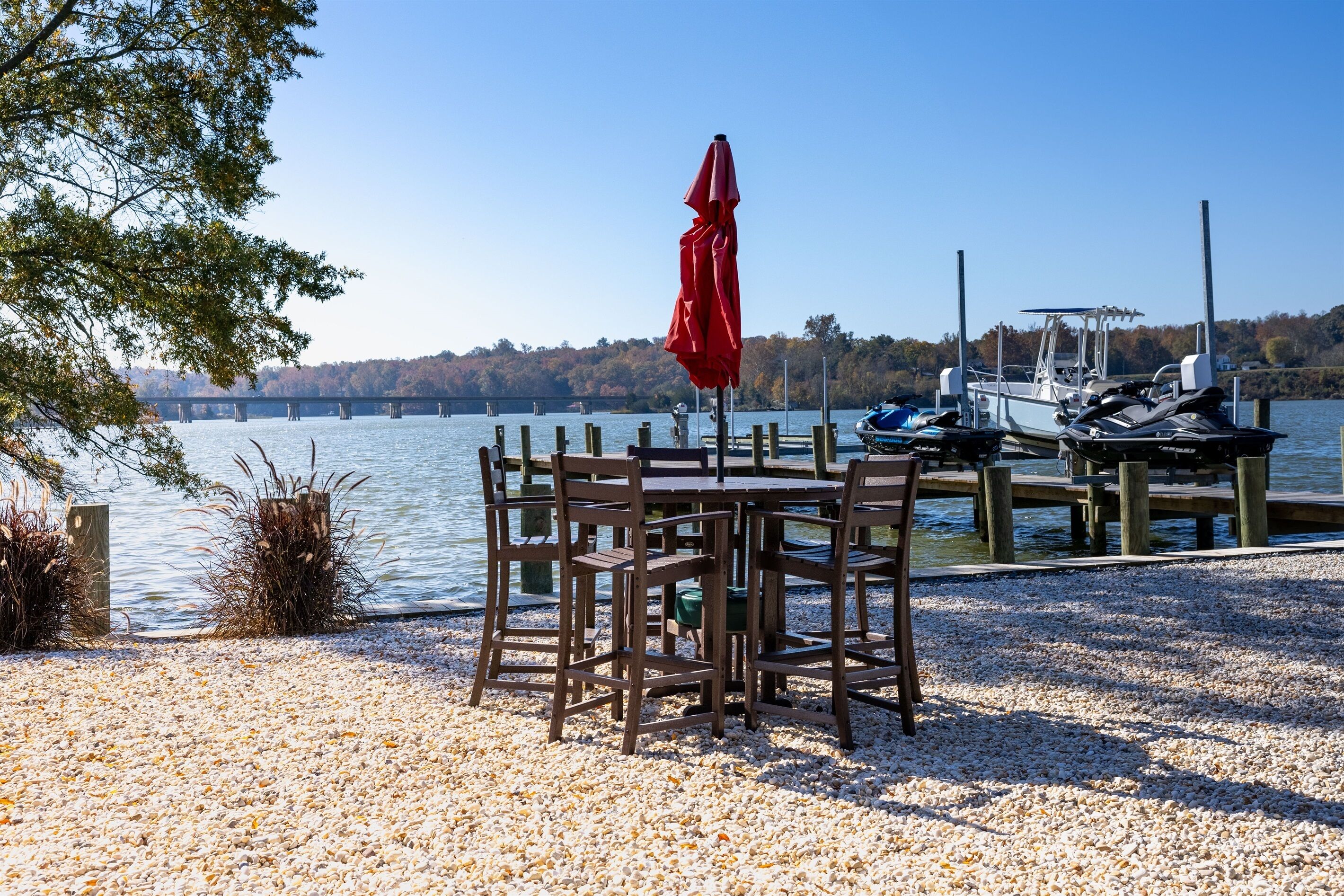 A wooden dock with boats, a table with chairs, and a red umbrella.