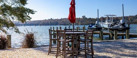A wooden dock with boats, a table with chairs, and a red umbrella.