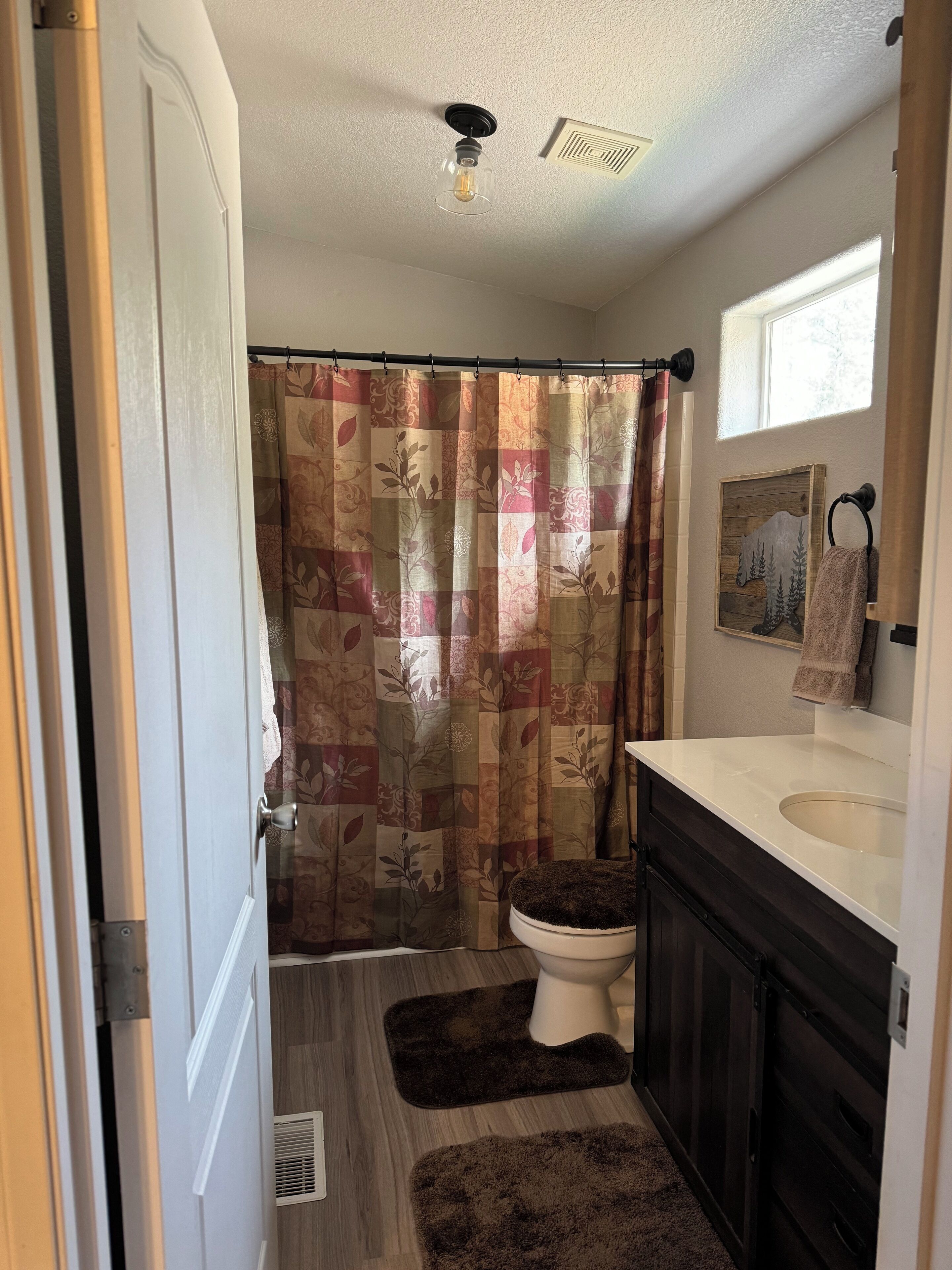 A bathroom with a shower curtain, toilet, sink, and wooden flooring.