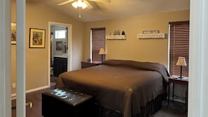 A bedroom with a bed, a ceiling fan, a nightstand, a lamp, and a wall-mounted shelf with decorative items.