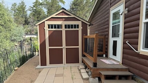 A wooden shed with a door and windows, a wooden deck, and a small set of steps leading to a door.
