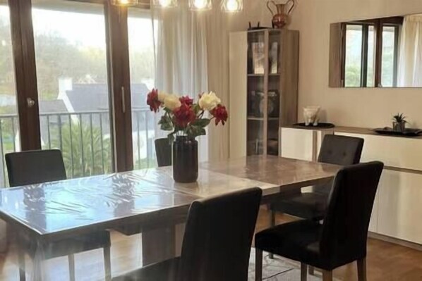 A dining area with a glass-top table, black chairs, and a vase of flowers.
