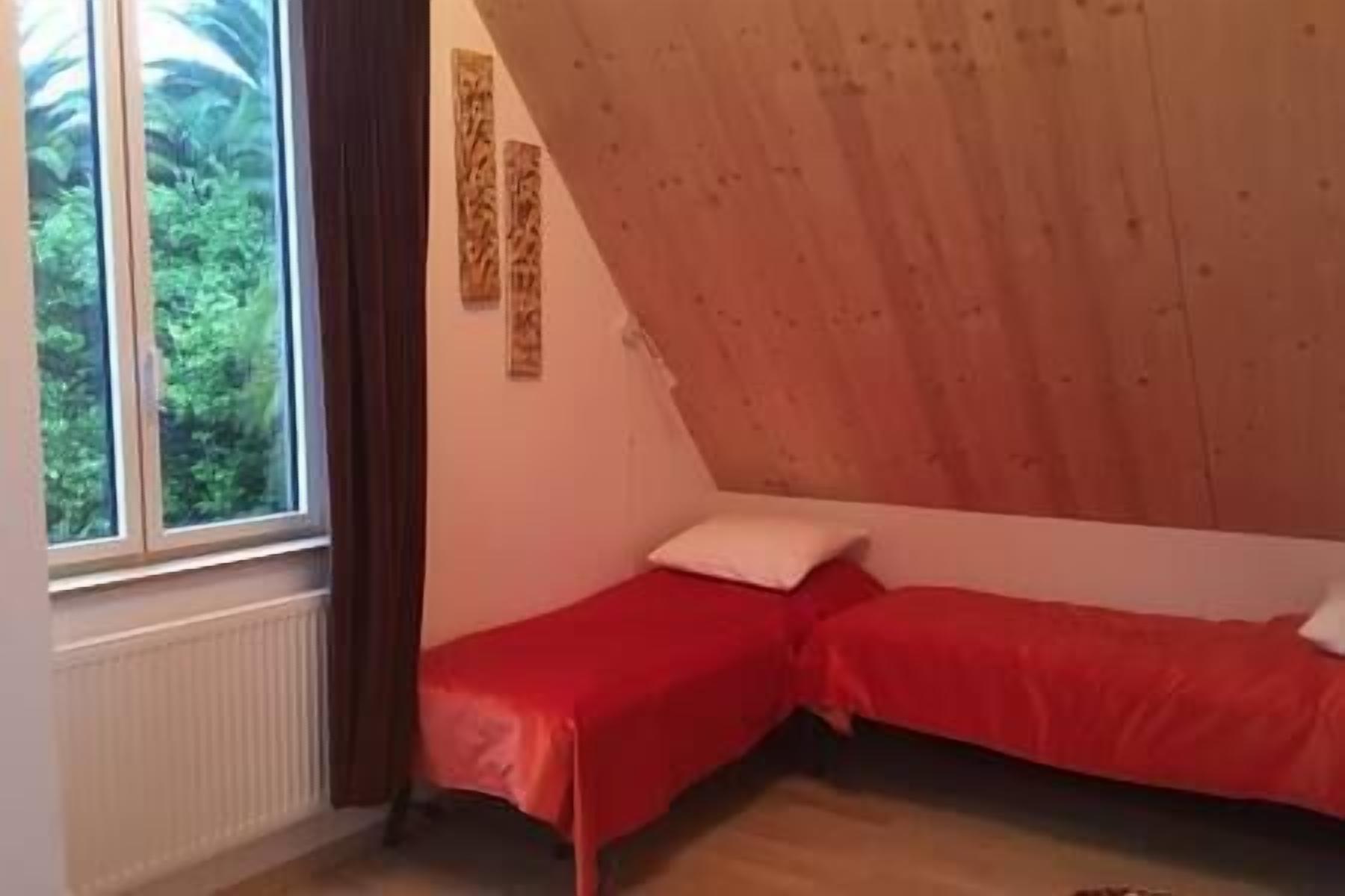 Une petite chambre avec deux lits simples, une fenêtre avec des rideaux et un radiateur.