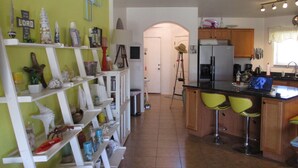 Une cuisine avec un mur vert, des étagères blanches, un coin bar avec des chaises jaunes et un réfrigérateur.