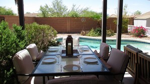 Une terrasse extérieure avec une table dressée pour le repas, entourée de chaises, et une piscine en arrière-plan.