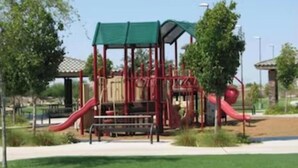 Une aire de jeux avec un toboggan rouge et une cabane de jeux dont le toit est vert.