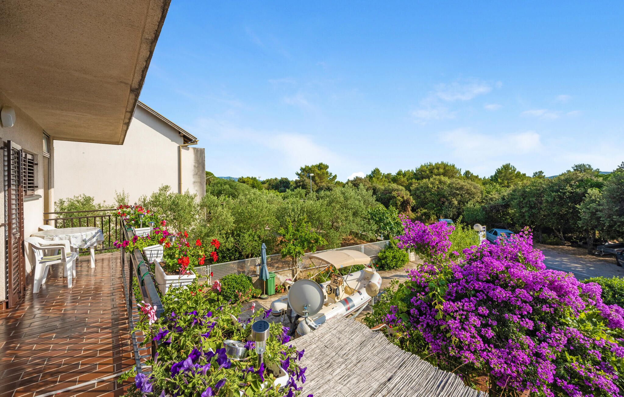 A balcony with a table and chairs, surrounded by vibrant flowers and a satellite dish.