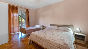Een slaapkamer met twee eenpersoonsbedden, een houten vloer, een groot raam met gordijnen en een nachtkastje met een lamp.