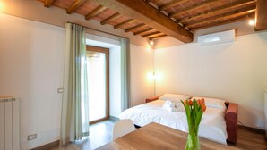 A hotel room with a wooden ceiling, a bed with white linens, a table with a vase of flowers, and a window with curtains. - Il Moro-Gemme del Casentino (Castel Focognano)