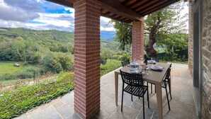 A covered patio with a table set for dining, overlooking a lush valley. - Il Moro-Gemme del Casentino (Castel Focognano)
