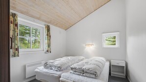 Een slaapkamer met een bed, nachtkastje, raam met gordijnen, wandlamp en radiator.