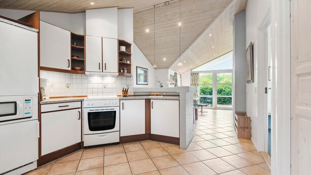 Een moderne keuken met witte kasten, een inbouwoven en een groot raam met uitzicht op groen.