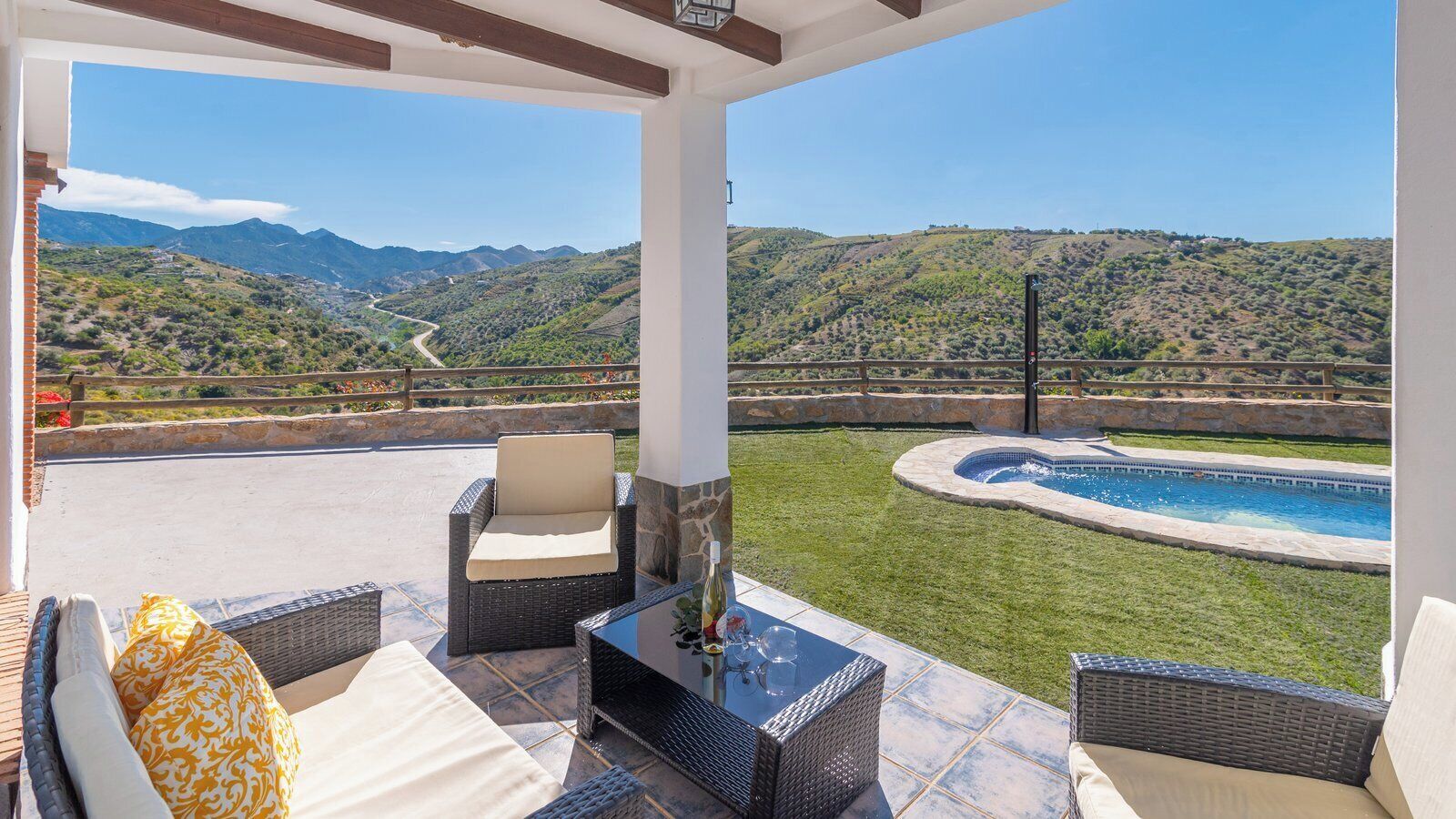 Un patio techado con muebles de mimbre, una piscina y vistas a las montañas.