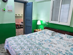 Una habitación con cama, mesita de noche, lámpara, ventana y puerta.