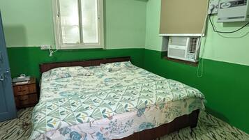 A room with a bed, a window, an air conditioning unit, and a wall-mounted electrical outlet.