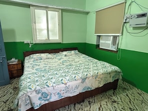 A room with a bed, a window, an air conditioning unit, and a wall-mounted electrical outlet.