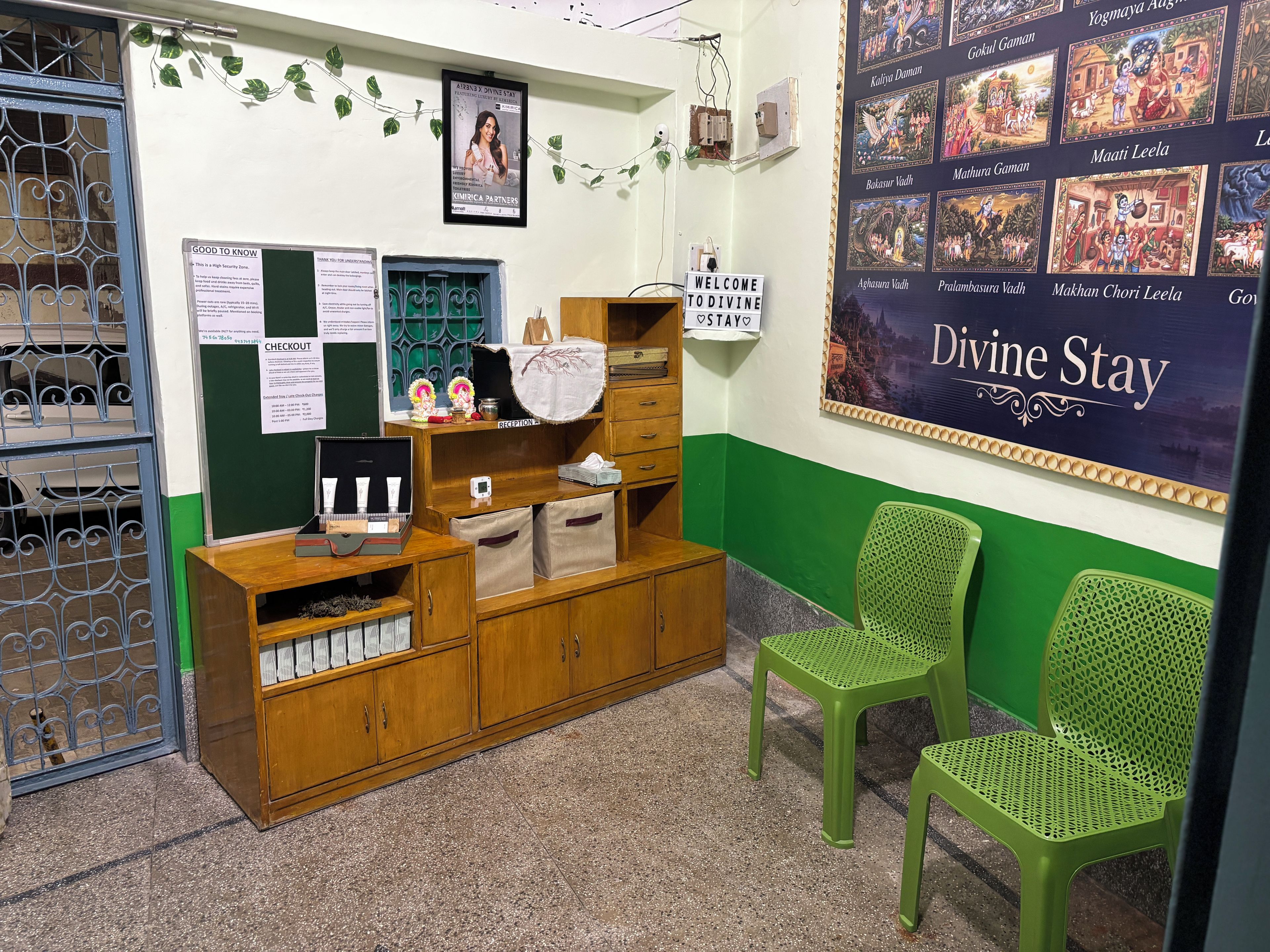 Un área de recepción con un escritorio de madera, sillas verdes, una pared con el letrero 'Divine Stay' y un cartel con varios nombres.