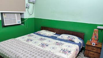 Una habitación con cama, mesita de noche, aire acondicionado instalado en la pared y ventana con persianas.