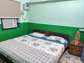 Una habitación con cama, mesita de noche, aire acondicionado instalado en la pared y ventana con persianas.
