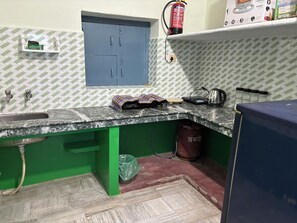 A kitchen with a marble countertop, green cabinets, a window, and a fire extinguisher on the wall. - Divine Stay At Krishna Janambhoomi Temple. Perfect For Family-Group. Sleeps 2-6 (Mathura)