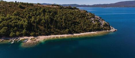 An aerial view of a coastal area with a forested peninsula, clear blue waters, and boats docked along the shore.