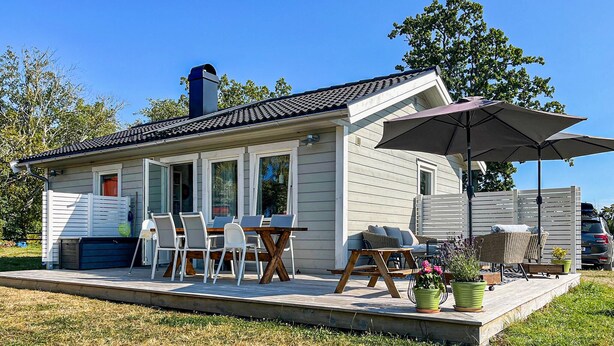 A small house with a patio, a dining table with chairs, and a large umbrella. - Stunning home in Gotland with kitchen (Gotland)