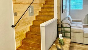 A wooden staircase with a metal handrail, a bench with a plant and a mouse figurine, and a modern living area with a sofa and a window. - The Eclectic - "treehouse" - B (Bryan)