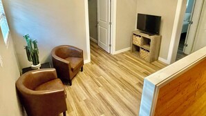 A living room with a wooden floor, a TV on a wooden stand, two leather chairs, and a door leading to another room. - The Eclectic - "treehouse" - B (Bryan)