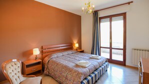 A hotel room with a bed, bedside tables, a chair, and a view of the outside through a large window.