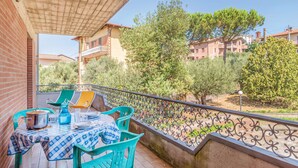 A balcony with a table set for dining, surrounded by a wrought iron railing, overlooking a residential area with trees and buildings.