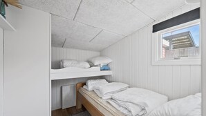 Een kleine kamer met een stapelbed, een raam met uitzicht op een gebouw en een klein vloerkleed.