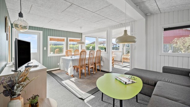Een moderne woonkamer met een grijze bank, een groene salontafel en een eethoek met houten stoelen en een tafel.