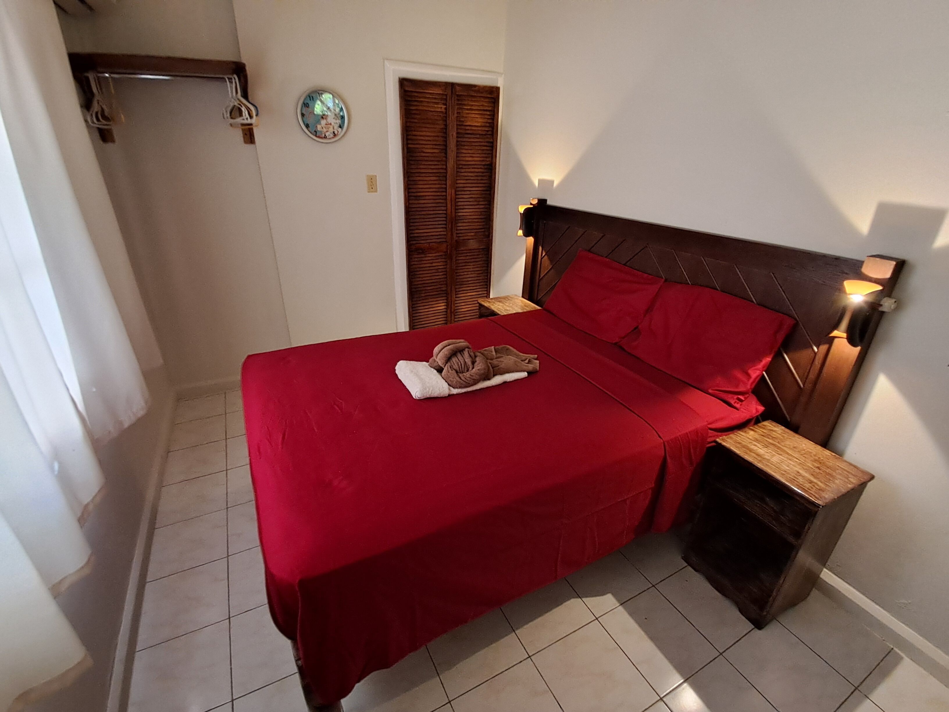 A bedroom with a red bedspread, wooden headboard, and a bedside lamp.
