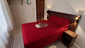 Un dormitorio con colcha roja, cabecero de madera y una lámpara de noche.